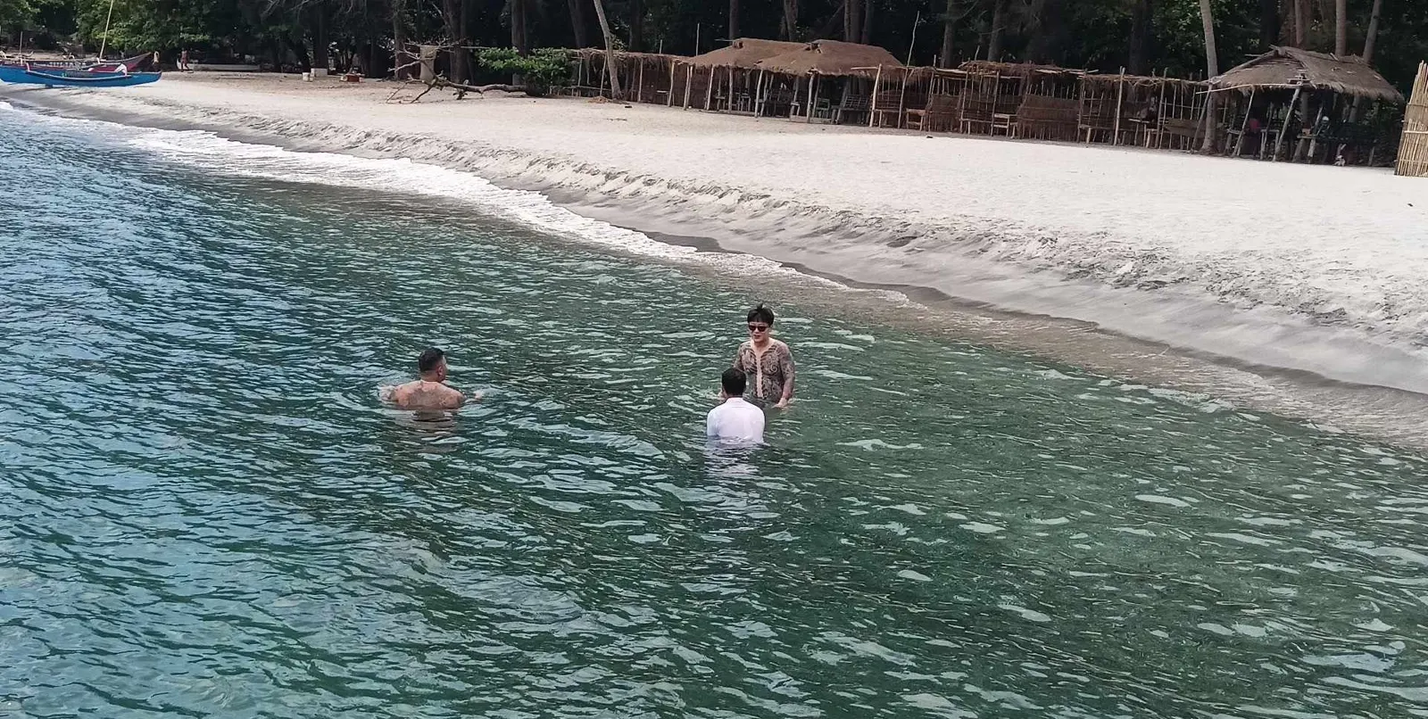 야자수와 비치 오두막이 있는 흰 모래 해변 앞에서 물놀이하는 여행객들